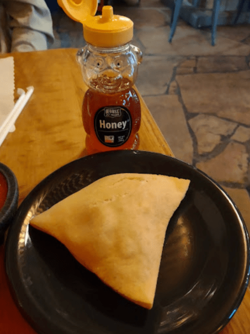 A plate with a triangular pastry next to a honey jar shaped like a bear on a wooden table.